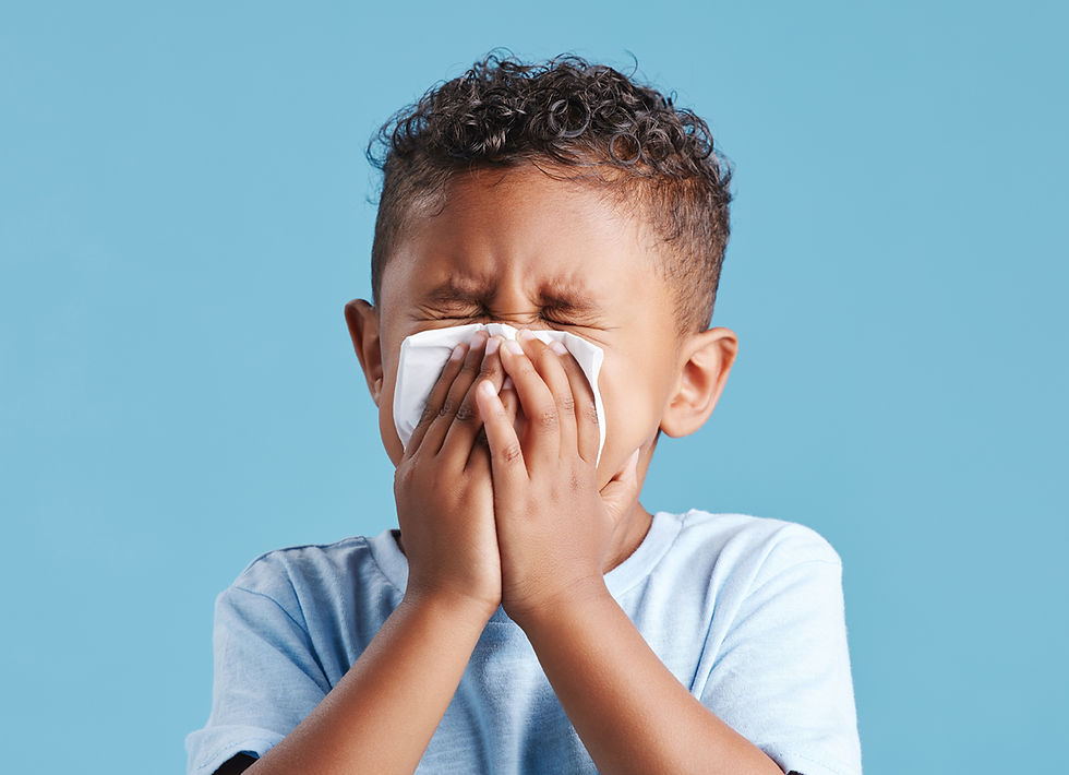 A child sneezes into a tissue, wearing a light blue shirt. Eyes closed, set against a solid blue background, conveying discomfort. Joyful Seeds Paediatric and Developmental Clinic located in Bukit Timah