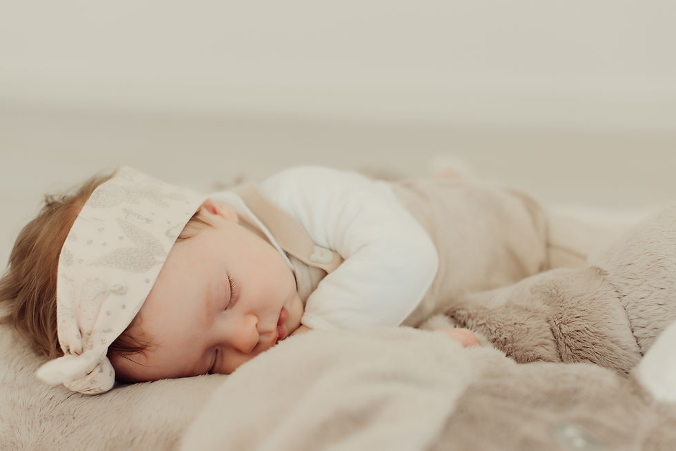 Sleeping baby in beige outfit and headband rests on a soft, fluffy surface. Neutral background evokes a sense of calm and coziness.