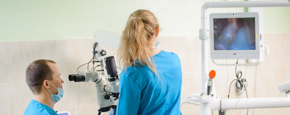 Two doctors uses a microscope, while a monitor displays a close-up view of the procedure.