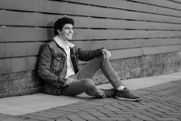 Black and white photo of St Charles North high school senior guy sitting and smiling, naturally posed and looking away from the camera.