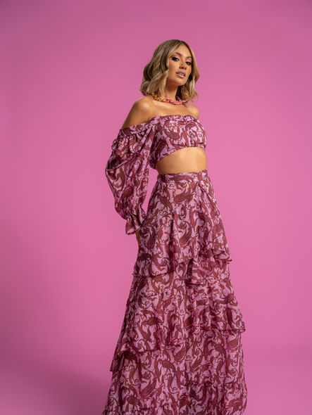 Γυναικείο μοντέλο με ροζ εμπριμέ crop top και μακριά φούστα, φωτογραφημένο σε ροζ φόντο στους χώρους της ImageNation