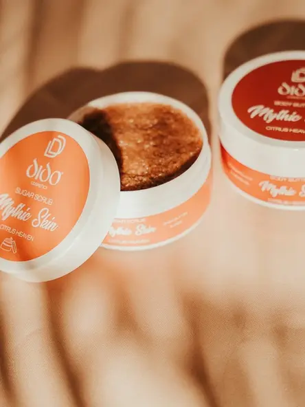 Sugar scrub και body butter Dido Cosmetics πάνω σε σατέν μπεζ ύφασμα με ζεστό φωτισμό.