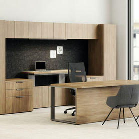 A workspace featuring a woodgrain desk with a metal frame, a matching storage hutch with integrated shelves, and a textured black backdrop. The space includes two modern guest chairs and a large window that provides natural light and city views.