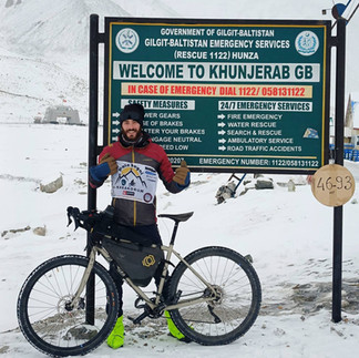 Ettore with his bike at the Khunjerab Pass sign in the Karakorum, surrounded by snow.