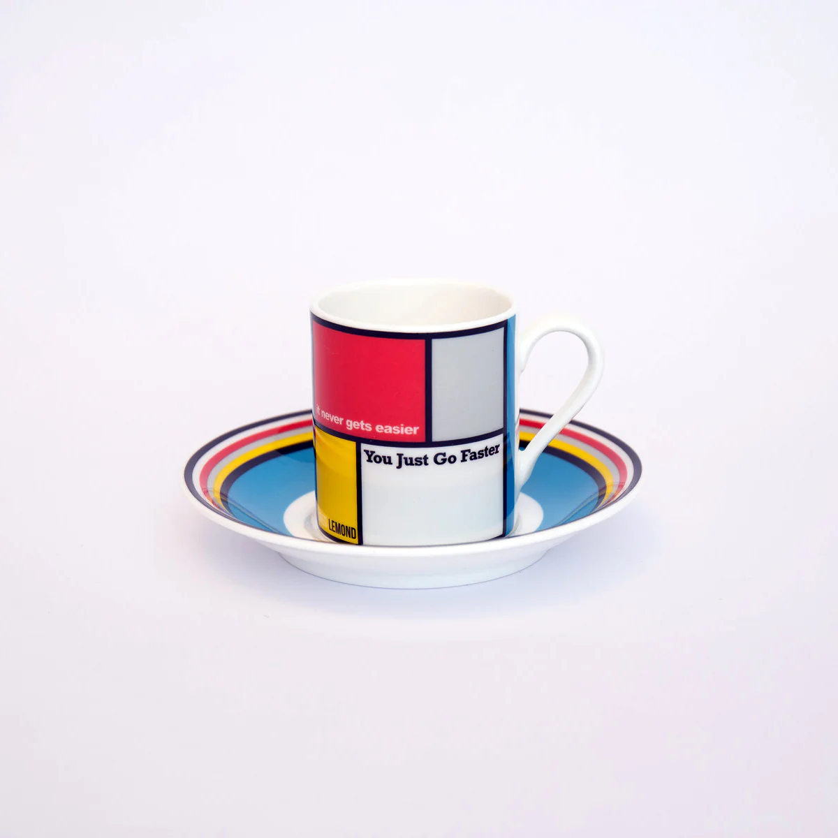 Greg LeMond-inspired fine bone china espresso cup and saucer by The Handmade Cyclist, featuring colorful geometric patterns and the quote 'It never gets easier, you just go faster.