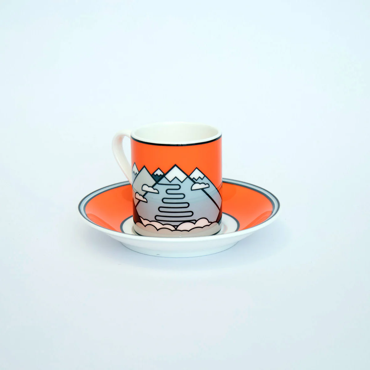 Passo Stelvio-themed fine bone china espresso cup and saucer by The Handmade Cyclist, showcasing an illustration of winding mountain roads and peaks on an orange background.