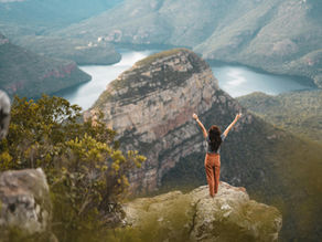 Person standing at the edge of a cliff at sunrise, symbolizing courage, reflection, and stepping into one’s growth edge while facing imposter syndrome.