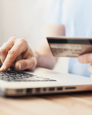 Close-up of hands typing on a laptop keyboard with one hand holding a credit card, illustrating online shopping or payment.