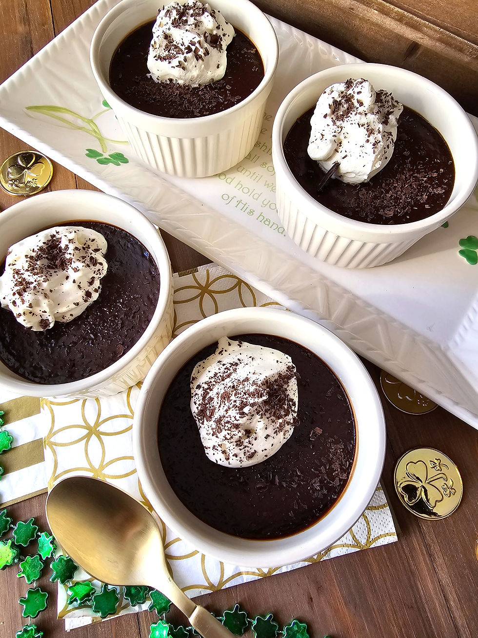 Four chocolate mint pots de creme desserts in white ramekins topped with whipped cream and chocolate shavings. Wooden table, green and gold decorations.