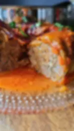 Close-up of a juicy stuffed cabbage topped with tomato sauce and herbs on a glass plate. The background is blurred, emphasizing the dish.