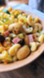 Macaroni salad with zucchini, ham, mushrooms, and carrots in a wooden bowl on a wooden surface. Bright colors create a fresh, vibrant look.