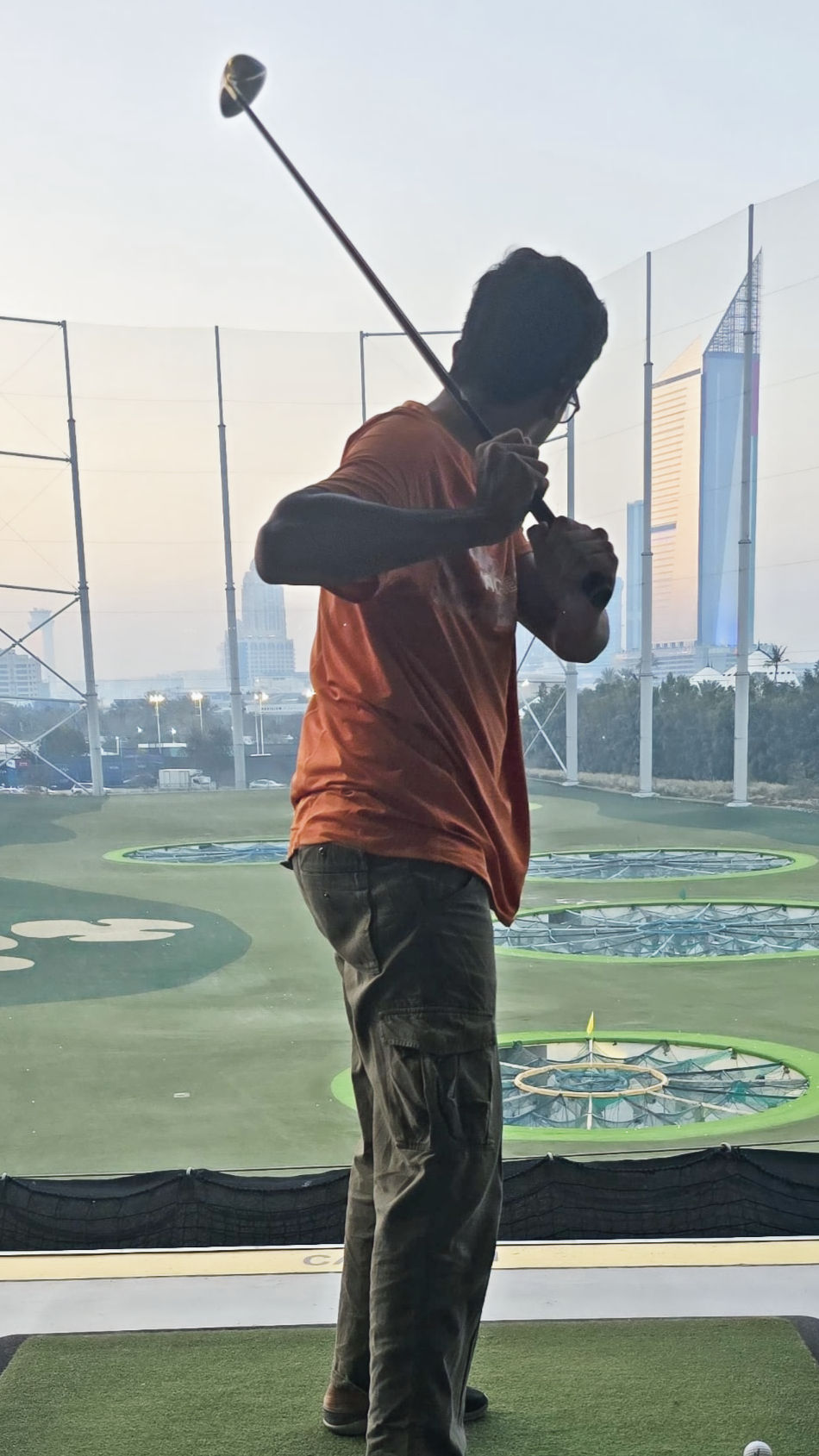 A boy playing top golf and swinging a shot