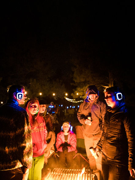 Campers gathered around a warm campfire, immersed in the silent disco vibes at Camp Disco, with glowing headphones lighting up the night.
