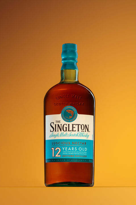 Product photographer Simon Eldon, bottle shot of single malt whiskey with pale blue label, studio lit against golden background.
