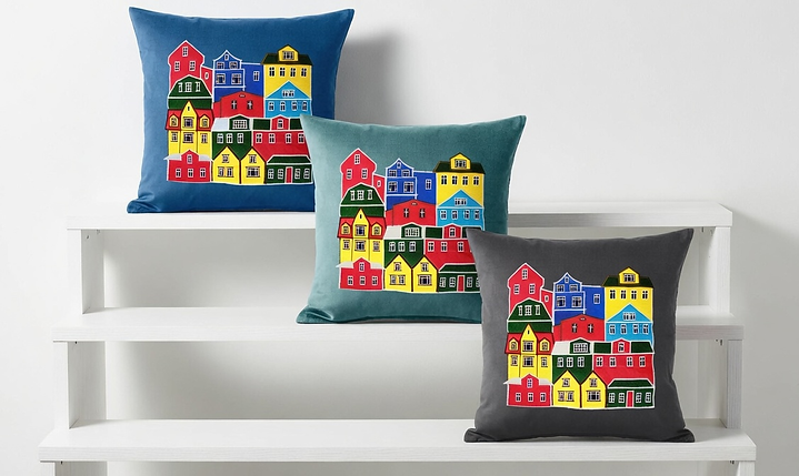 A set of three decorative cushions in navy blue, teal, and charcoal gray, each featuring a colorful embroidered scene of traditional Reykjavik houses on white display shelves.