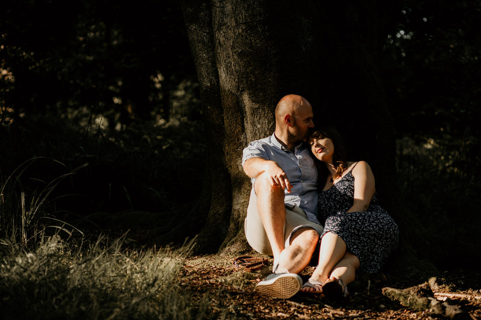 Couple having a cuddle under a tree in the evening sun on their engagement shoot at Stourhead, wiltshire. Photography by Louisa Jane 