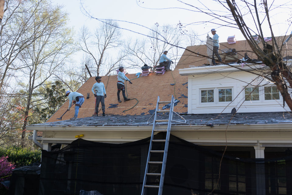 10 or more crew members work to remove the old house shingles. Roof replacement cost calculations depend on the size of the house.