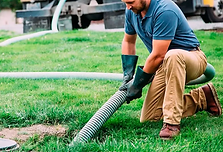 Homem usando equipamento de proteção, limpando uma fossa séptica em uma fazenda, manuseando uma mangueira conectada a um cami