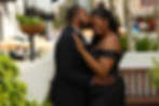 Man in black suit kissing woman's forehead outdoors.