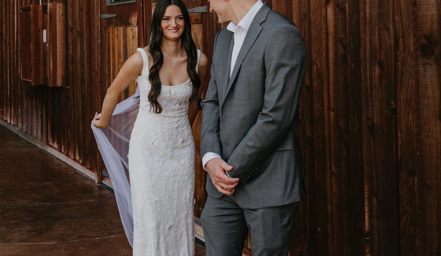 Bride and groom pose by wooden barn; Leah and Anthony's Summer Wedding at Tucannon Cellars.