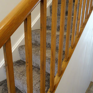 Grey heathered carpeted staircase with a polished wooden banister and spindles against white walls