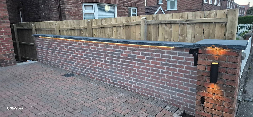 Low brick boundary wall with integrated coping lighting next to a herringbone block paved driveway