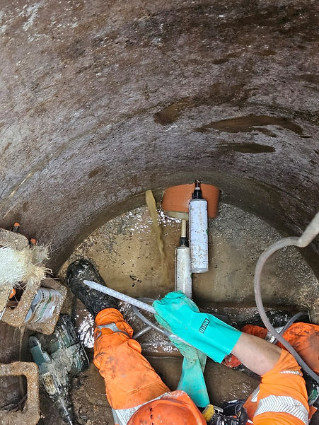 Looking down into a circular manhole where an engineer in green gloves is preparing grout injection equipment
