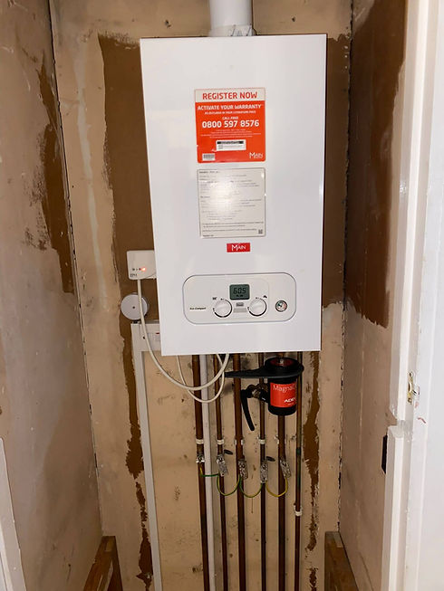 Newly installed white gas boiler with pipes and magnetic filter in an unfinished alcove