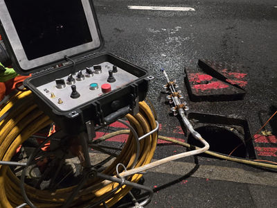 CCTV drainage survey equipment with a monitor and yellow cable reel set up next to a manhole on a road at night