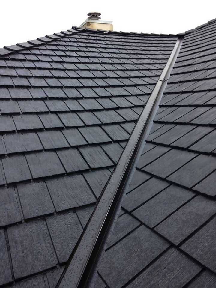 A close-up view of a sloped roof covered in dark shingles, showing the ridges and valleys where the shingles meet.