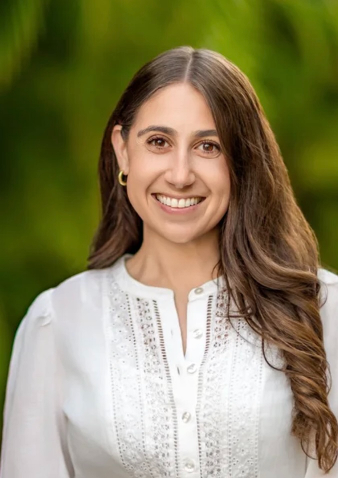 Woman with brown hair smiling. wearing a white blouse and golden hoop earings