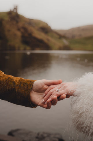 Close up detail of bride and groom holding hands showing engagement ring