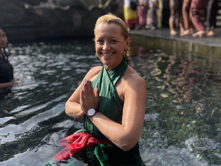 Mehala Beckett, sitting in a river, smiling at the camera while her hands are in a prayer position.