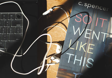 Paperback book So It Went Like This by C. Spencer alongside a laptop and headphones