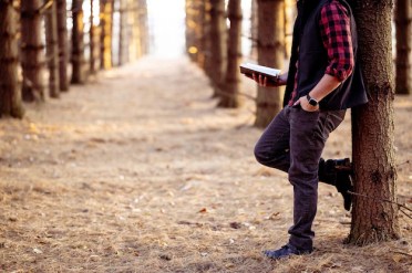 Free photo shot of a man holding a book posing in a forest