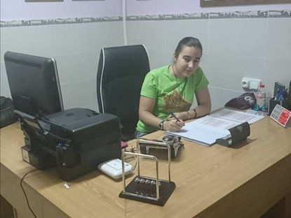 Carmen Galvañ con camiseta verde escribe en un escritorio de oficina; detrás hay diplomas enmarcados y un ambiente tranquilo.