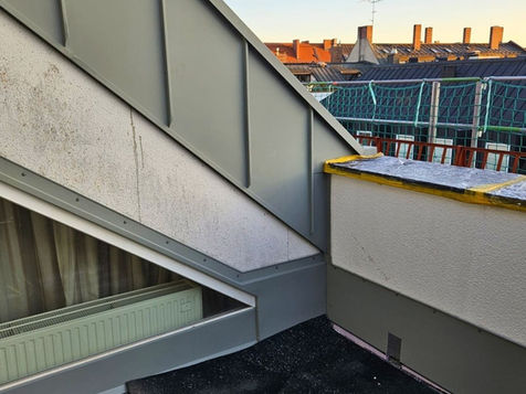 Dachanschluss mit grauer Metallverkleidung zwischen Flachdach und geneigtem Dach