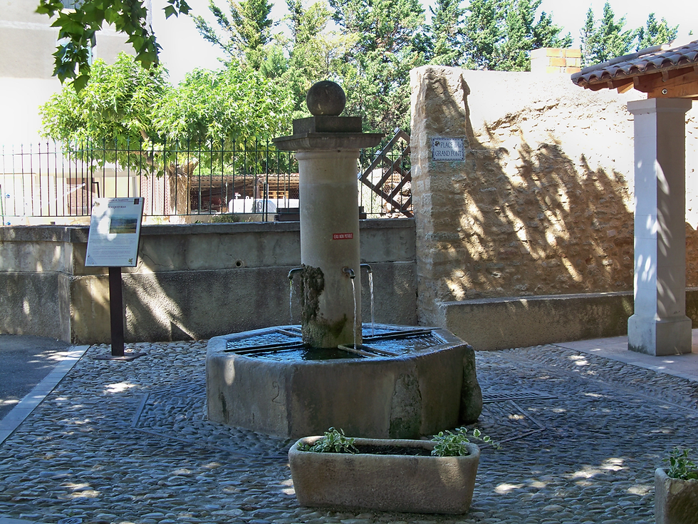 Steinerner Dorfbrunnen auf der Place de la Grand Font in Vacqueyras, ein historischer achteckiger Wasserbecken aus Naturstein mit zentraler Säule vor einer alten Natursteinmauer im Departement Vaucluse, Provence.