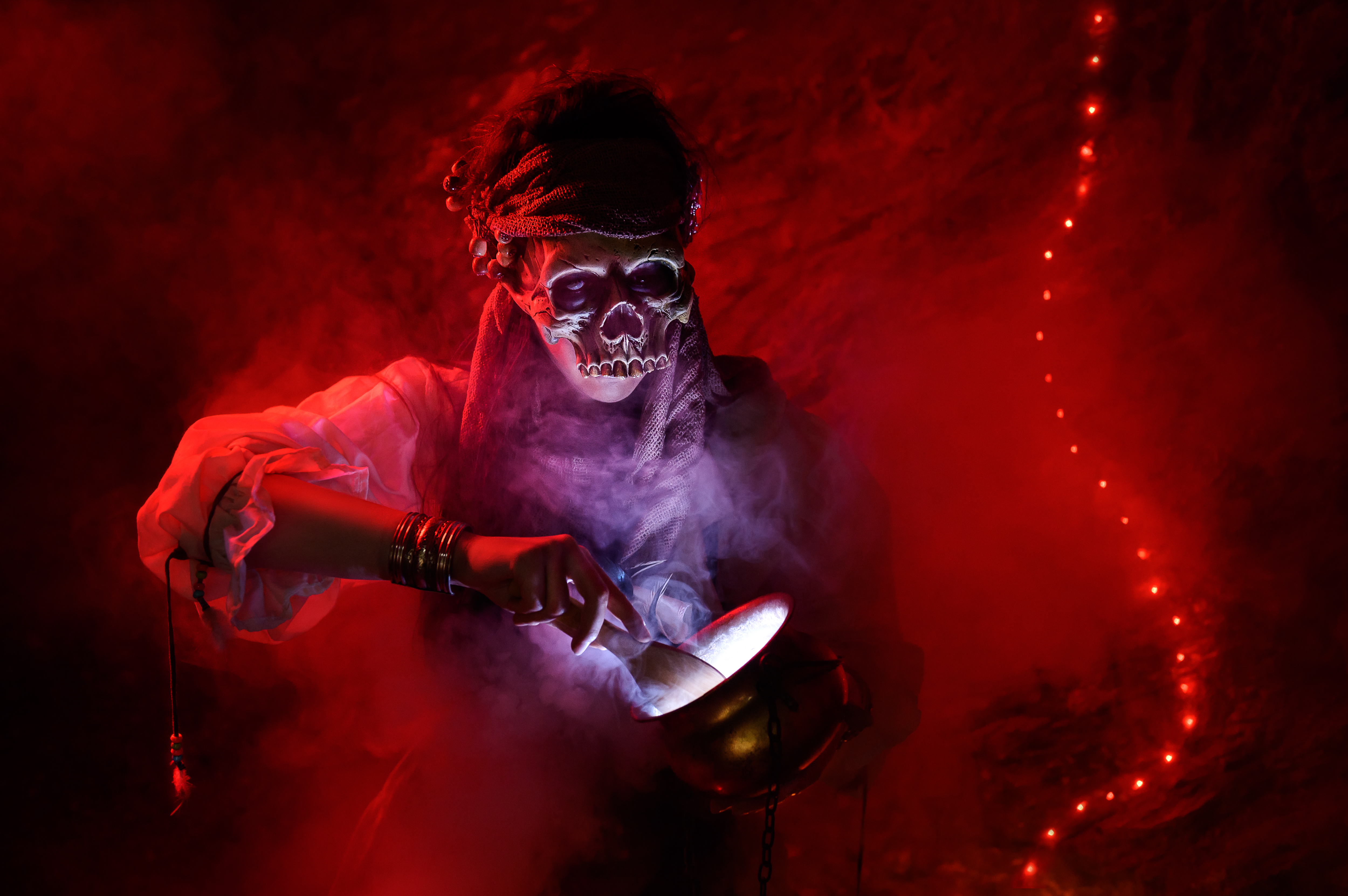 Voodoopriestess preparing potions in her cave while wearing a skullmask.