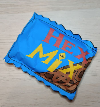 a small blue pouch of paper filled with "snacks". HEX MIX is written in red and yellow letters on top. In the right lower corner are small pretzesl visible. It's a fake snack from the Show The Owl House, recreated in paper.