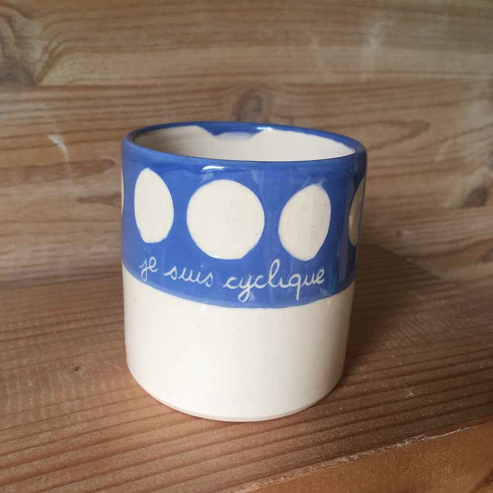 un mug ceramique avec les phases lunaires sur fond bleu ciel et une écriture à la main "je suis cyclique"