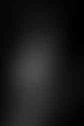 A dramatic black and white maternity portrait by Michael Anthony at My Canvas Portraits, capturing a side profile of a pregnant individual embracing her belly, surrounded by darkness that accentuates the curves and form of her figure.