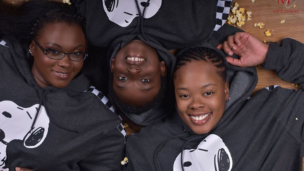 African-American mother, child, and auntie smiling in matching Snoopy hoodies with popcorn scattered on the floor.