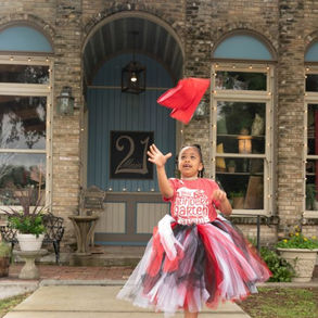 Little girl in red tutu dress tossing graduation cap outside vintage building