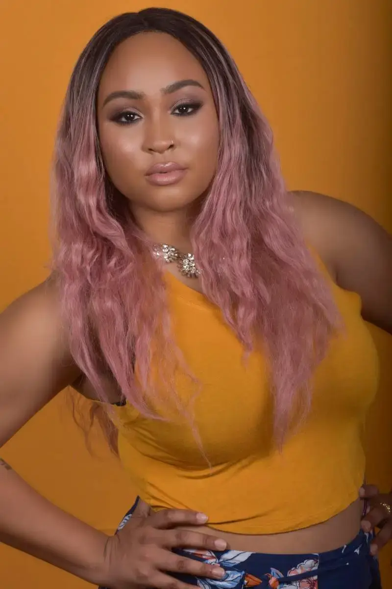 A confident woman with soft glam makeup and pink wavy hair poses against a warm mustard backdrop. Her glowing skin and subtle contour highlight her natural beauty. This portrait captures the balance of strength and softness that defines the self-love journey. Professionally styled and photographed by Jessica Blends for My Canvas Portraits in Killeen, Texas.