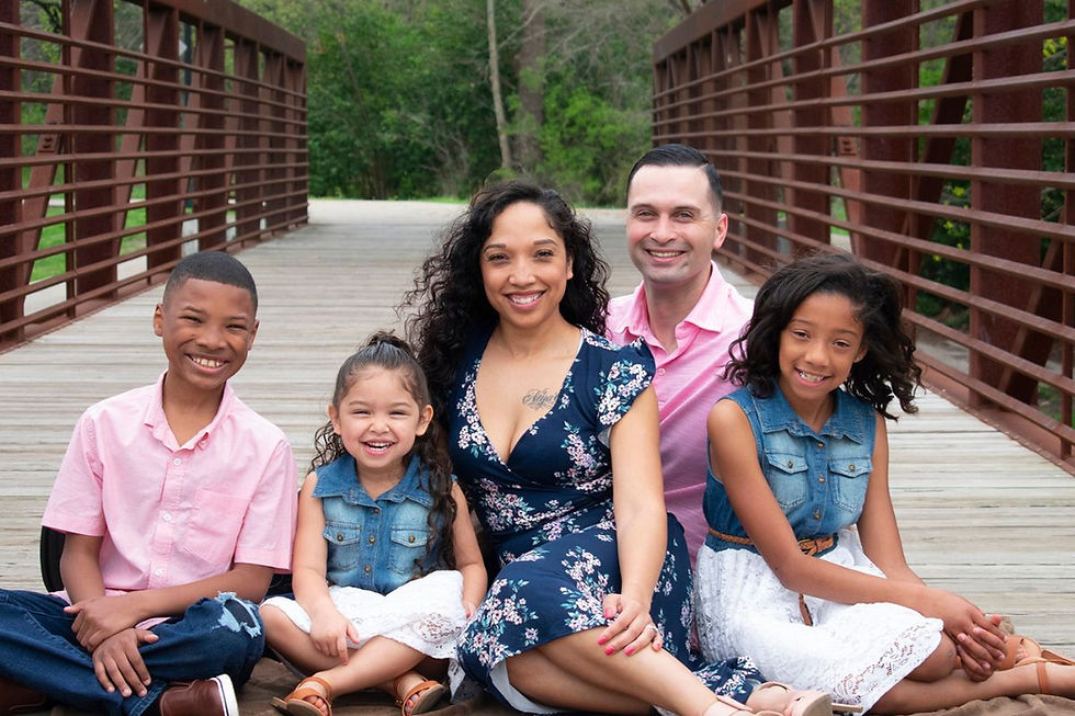A family of five sits together on a walking bridge during a family photo shoot in Austin, TX. The parents and kids are close, smiling naturally, and clearly comfortable in the moment. This image shows how movement-based family sessions help kids relax and engage without pressure. Outdoor Austin locations like this bridge provide space for families to settle in and connect. The photo reflects real expressions instead of stiff posing.
