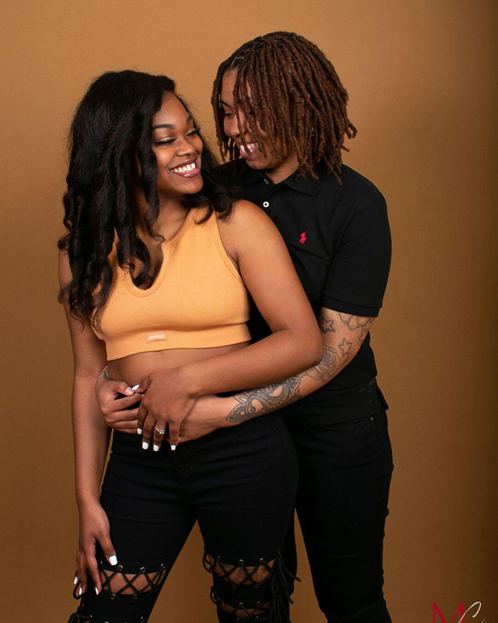 Lesbian couple wearing coordinated orange and black outfits smiling during a casual studio portrait