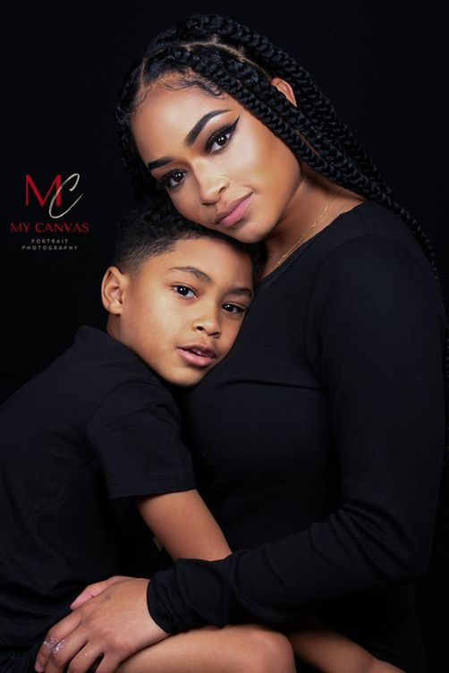 Mother and young son wearing black outfits posing closely together in a studio portrait.
