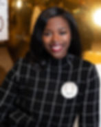 Smiling woman in black checkered sweater with a badge reading "Mkali." Warm, golden background, positive and professional atmosphere.