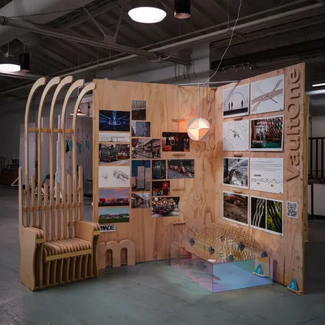 A plywood display board with images of architectural and fabrication projects on them. A seat made of plywood sits beside it.